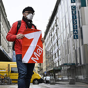 Demonstrant am 1. Mai 2021 mit FFP2-Maske und 1.-Mai-Plakat in leerer Genfer Strasse