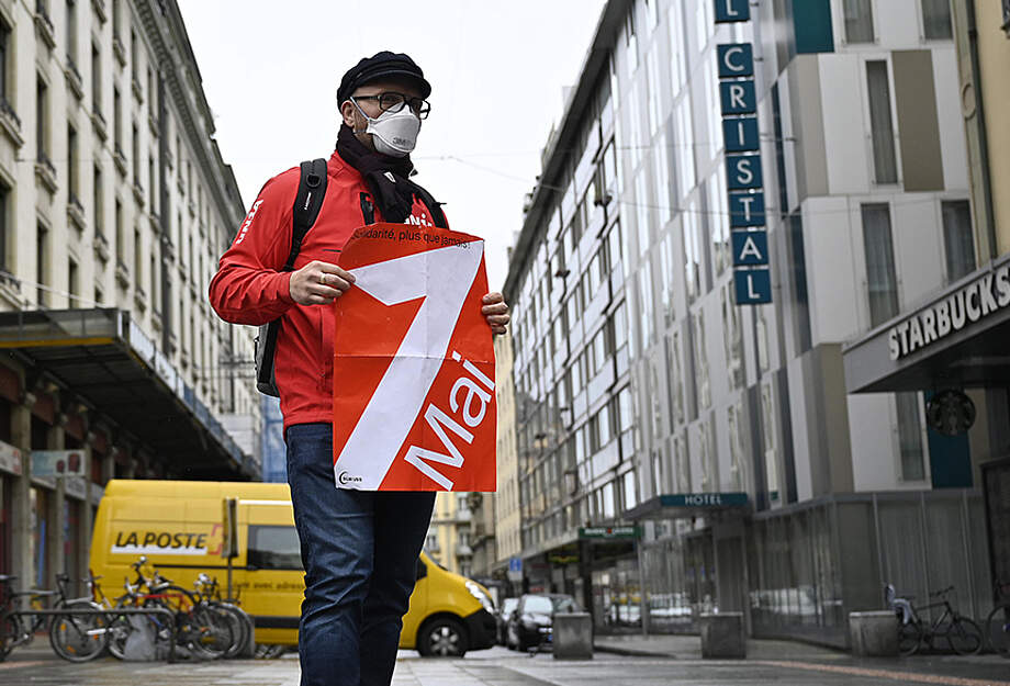Demonstrant am 1. Mai 2021 mit FFP2-Maske und 1.-Mai-Plakat in leerer Genfer Strasse