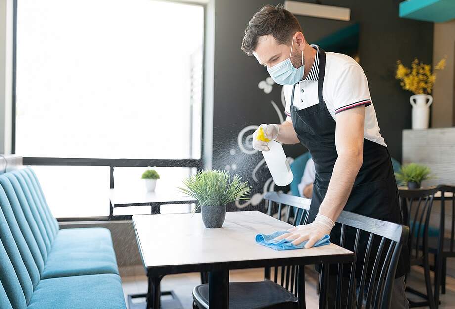 Mitarbeiter mit Maske reinigt Tisch in der Gastronomie