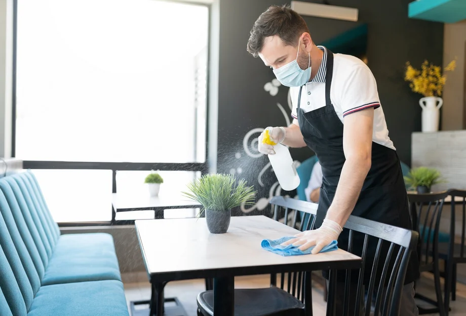 Mitarbeiter mit Maske reinigt Tisch in der Gastronomie