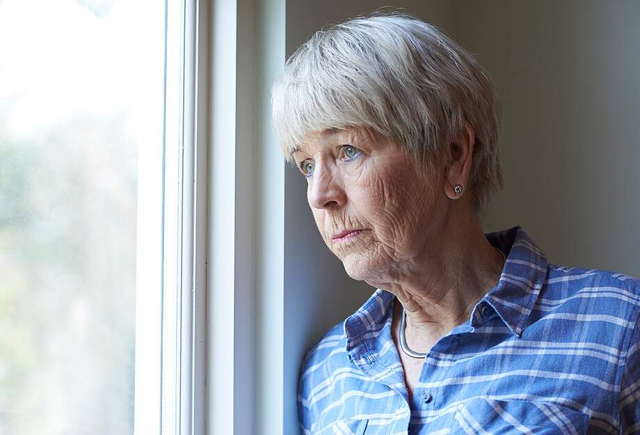 Ältere Frau schaut traurig aus dem Fenster