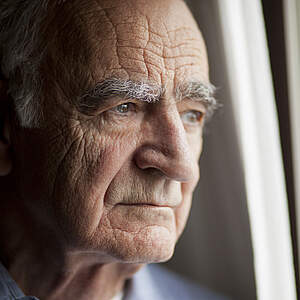 Alter Mann schaut nachdenklich aus dem Fenster